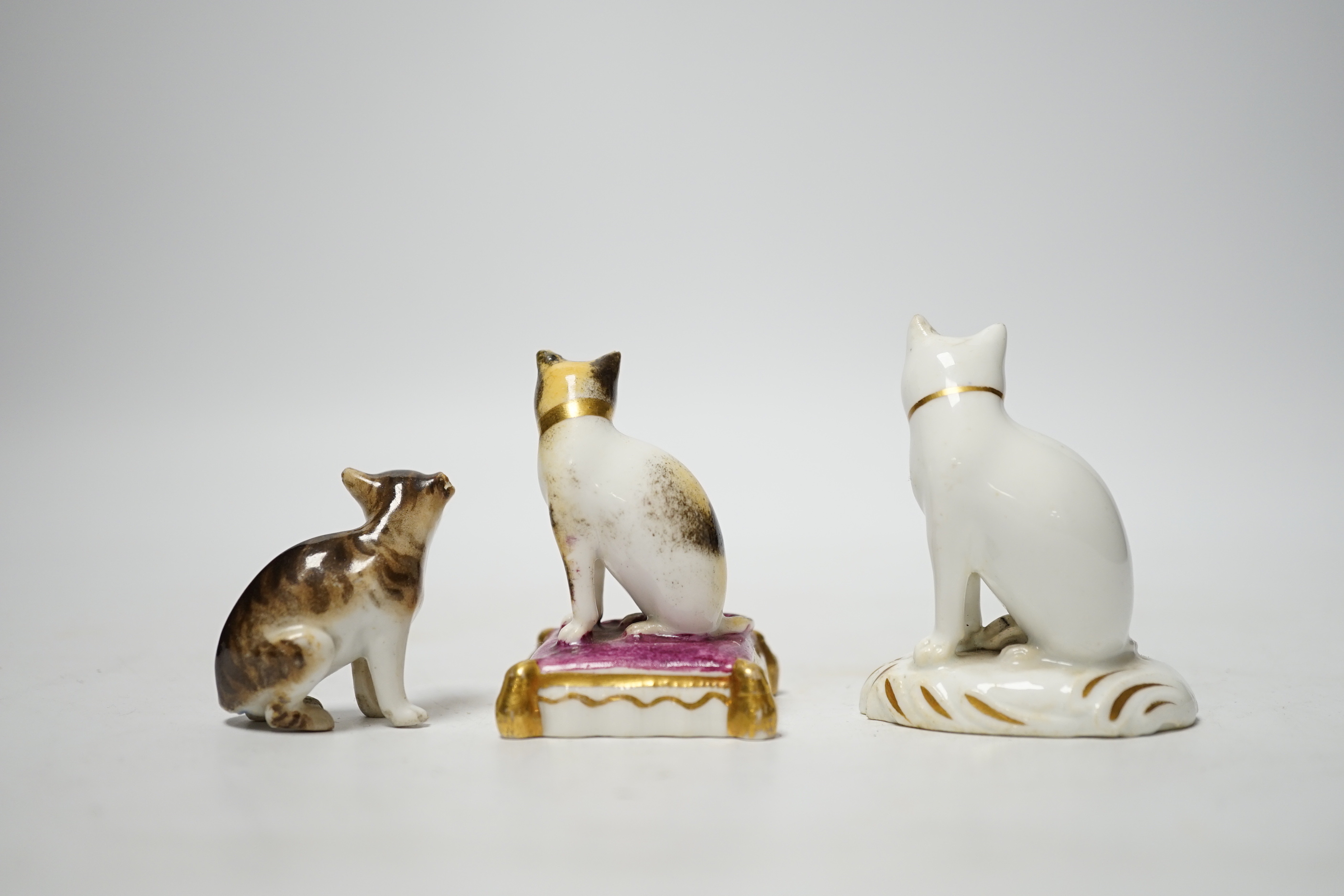 Two Rockingham porcelain models of seated cats, c.1830, the cat seated on a maroon cushion with impressed Rockingham Mark and incised model number 17, 5.3cm high, the white and gilt example with incised model number 11,